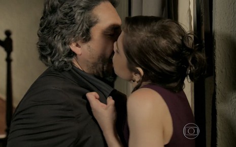 José Alfredo (Alexandre Nero) é segurado pelo colarinho do blazer enquanto recebe um beijo de Cora (Drica Moraes) em cena de Império