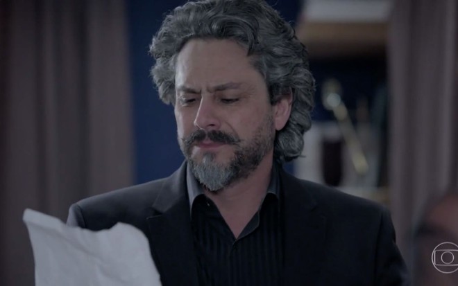 O ator Alexandre Nero como o personagem José Alfredo olha sério para uma folha de papel em cena da novela Império, da Globo