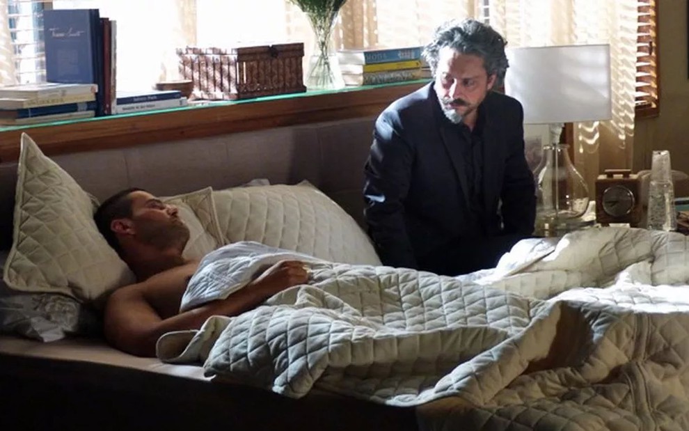 Maurílio (Carmo Dalla Vecchia) deitado na cama com José Alfredo (Alexandre Nero) sentado ao lado em cena da novela Império