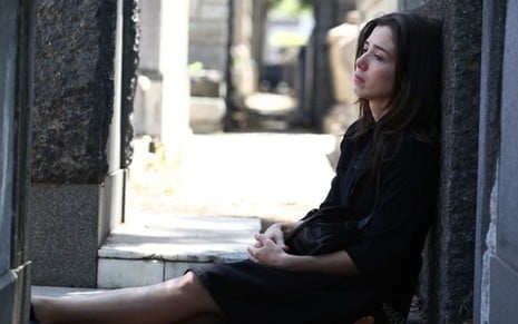 Marjorie Estiano em cena de Império: atriz está caracterizada como Cora, sentada em cemitério e veste roupas pretas