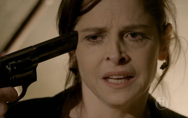 Drica Moraes grava com expressão de desespero e com uma arma apontada para sua cabeça como Cora de Império