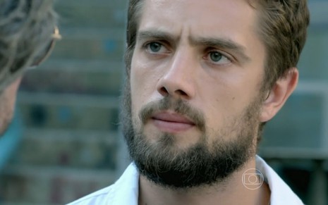 Rafael Cardoso grava vestido de branco, com barba e cenho franzido como Vicente de Império, reprise da Globo