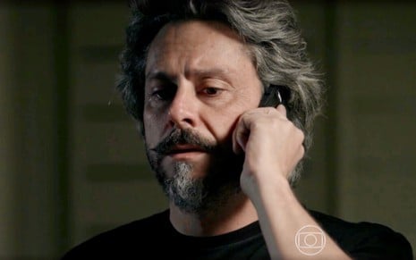O ator Alexandre Nero usa camiseta preta e simula fazer ligação pelo celular em cena de Império, da Globo