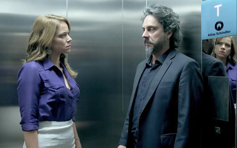 Cristina (Leandra Leal) está de blusa roxa e saia branca dentro de um elevador diante de José Alfredo (Alexandre Nero) em cena de Império