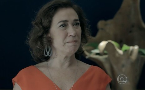 Maria Marta (Lilia Cabral) está em pé, usa um vestido vermelho e chora na sala da mansão dos Medeiros em cena de Império