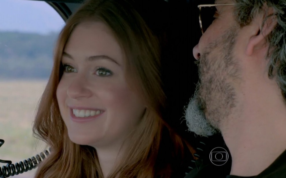 Marina Ruy Barbosa grava sorridente em helicóptero ao lado de Alexandre Nero como Maria Isis e José Alfredo de Império