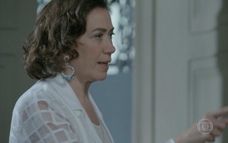 Lilia Cabral grava vestida de branco, com brinco luxuoso e expressão de fúria como Maria Marta de Império