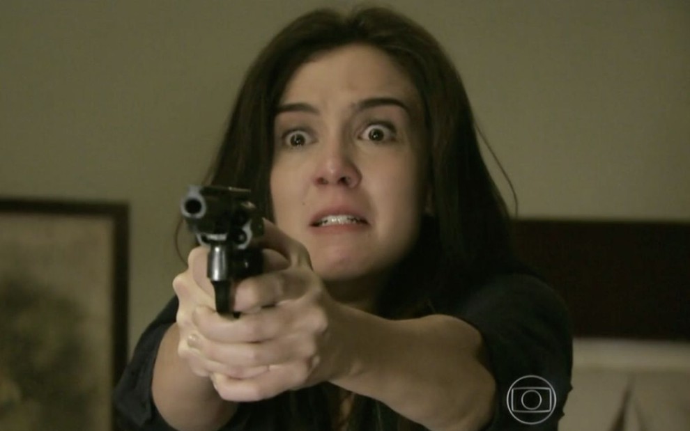 A atriz Marjorie Estiano caracterizada como a personagem Cora segura uma arma e faz cara de louca na novela das nove da Globo Império