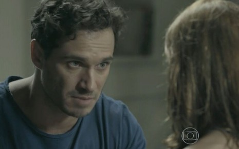 Orville (Paulo Rocha) está sentado em sofá na sala da sua casa; ele conversa com Helena (Julia Fajardo), que está está de costas
