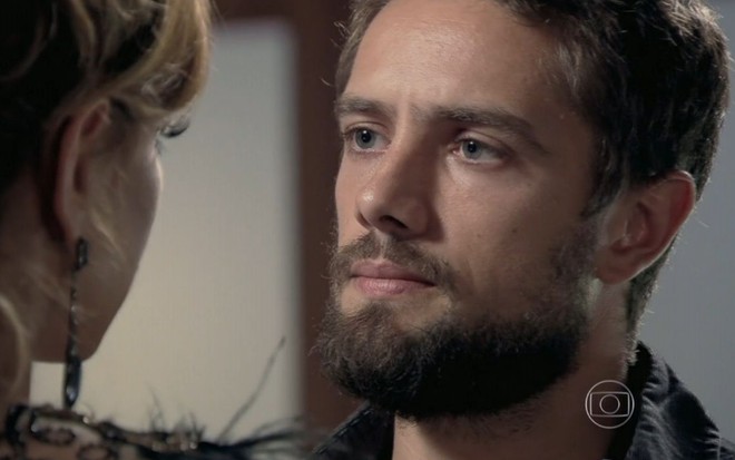 Rafael Cardoso grava cena com expressão séria olhando para Leandra Leal, que aparece de costas na imagem, como Vicente e Cristina