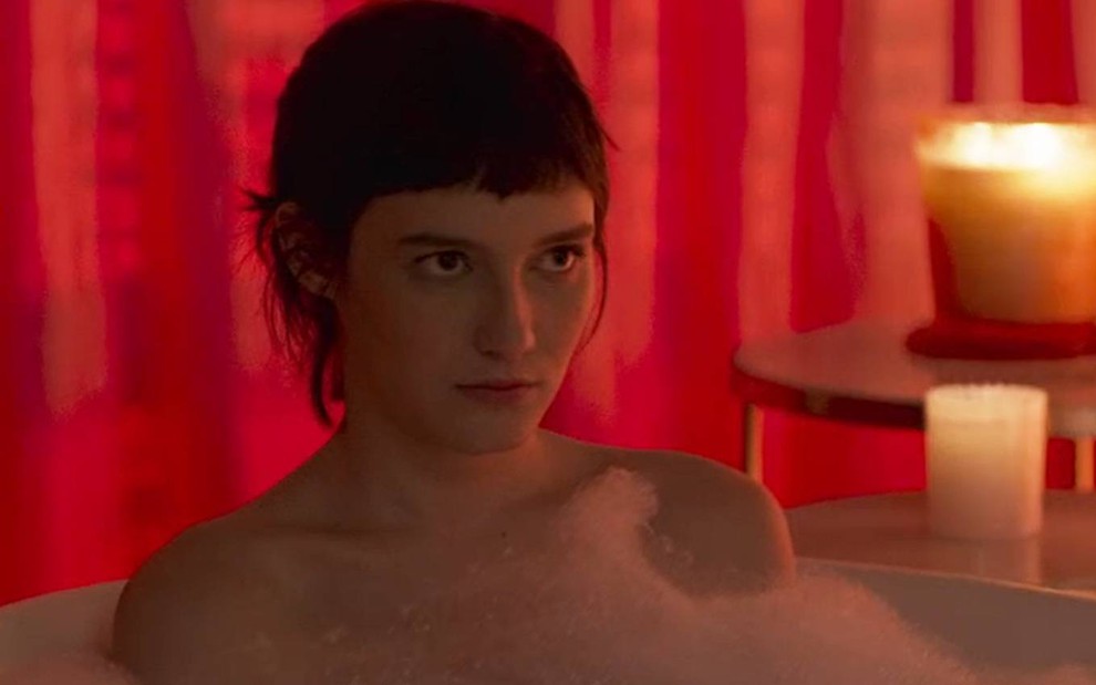 Nina Tomsic surge em banheira de espuma e olha para frente com cara de séria em cena de Quanto Mais Vida, Melhor
