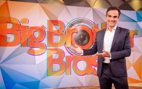 O apresentador Tadeu Schimidt sorri na frente de telão com o logo do Big Brother Brasil, da Globo