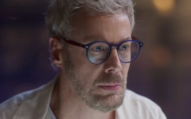 Ator Guilherme Weber olha para frente com cara de sério em cena de Cara e Coragem
