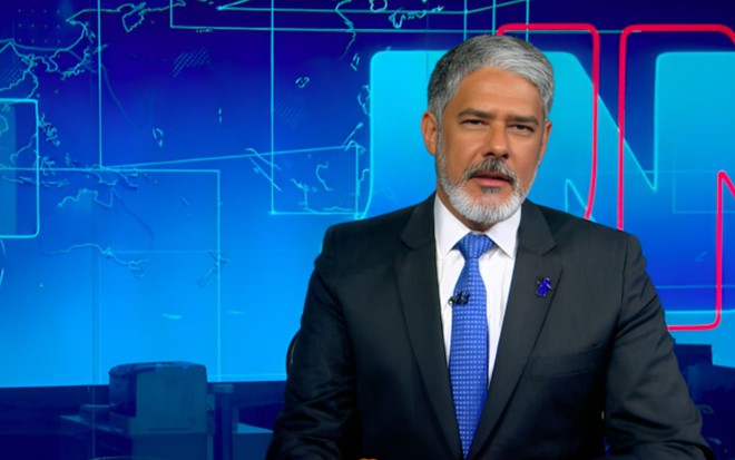 William Bonner com um broche azul do Criança Esperança no paletó preto no estúdio do Jornal Nacional