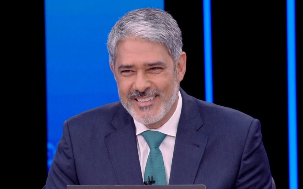 William Bonner com uma gravata azul e sorriso durante entrevista com Jair Bolsonaro