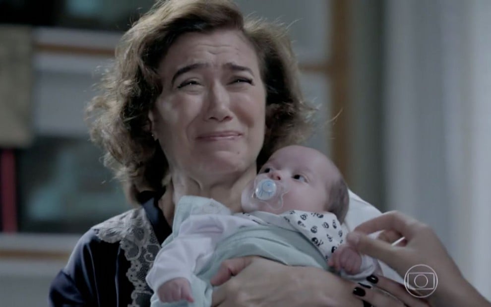 A atriz Lilia Cabral, caracterizada como a personagem Maria Marta, faz cara de novo segurando um bebê em cena da novela das nove Império, da Globo