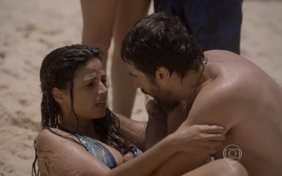 Emanuelle Araújo grava com cabelo molhado, deitada na areia e nos braços de Eriberto Leão como Dandara e Gael de Malhação