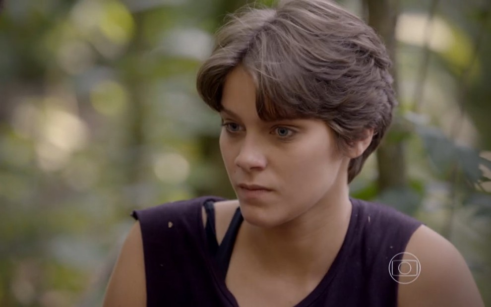 Isabela Santoni, a Karina de Malhação, usa uma camisa preta e olha desconfiada para alguém. Ela usa um cabelo curto