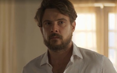 Sergio Guizé, caracterizado como José, tem a expressão séria e concentrada; ator veste camisa social branca