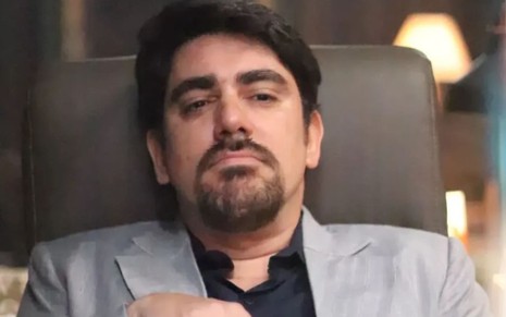 Marcelo Adnet caracterizado como Noé Dantas; ele usa uma camisa social preta e um blazer cinza. O semblante esta desafiador em cena de Mar do Sertão