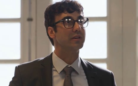 Gabriel Godoy caracterizado como Márcio Castro; ator usa terno preto e óculos em cena de Mar do Sertão