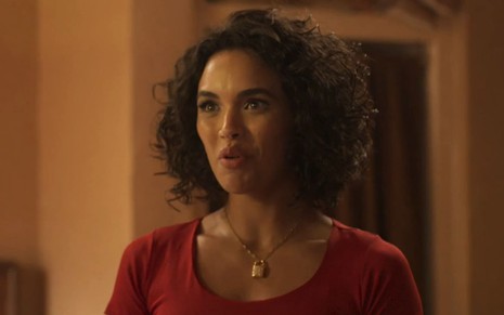 Giovana Cordeiro caracterizada como Xaviera; atriz usa um vestido vermelho e exibe deboche em cena de Mar do Sertão