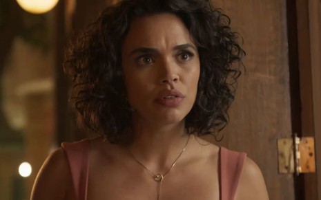 Giovana Cordeiro caracterizada como Xaviera; atriz usa um vestido vermelho e tem a expressão séria em cena de Mar do Sertão
