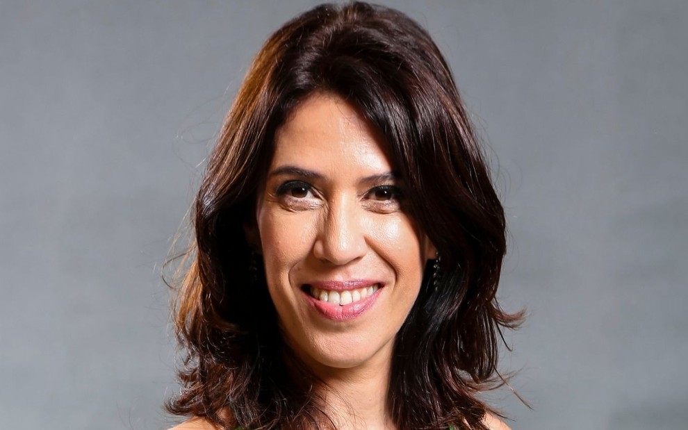 Maria Clara Gueiros em foto de divulgação: atriz está com vestido verde estampado de alças, cabelo solto no ombro e sorri para a câmera