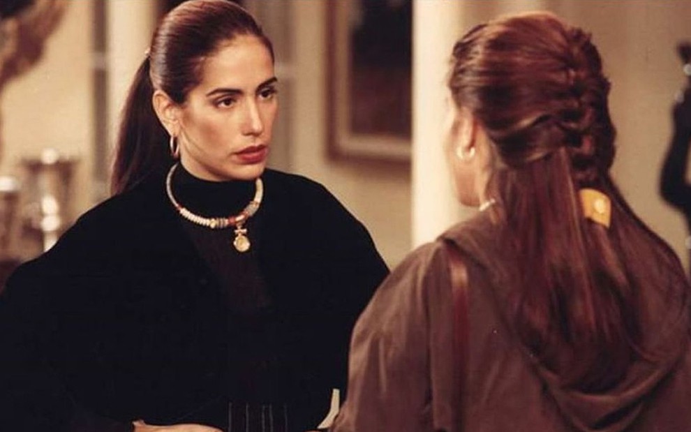 Gloria Pires em cena como as gêmeas Ruth (de costas) e Raquel, usando blusa preta