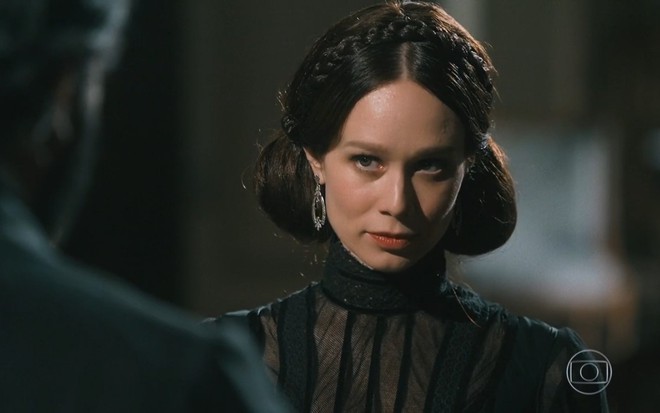 Mariana Ximenes grava vestindo preto, com cabelo preto e expressão de nervoso e sem graça como Luísa de Nos Tempos do Imperador