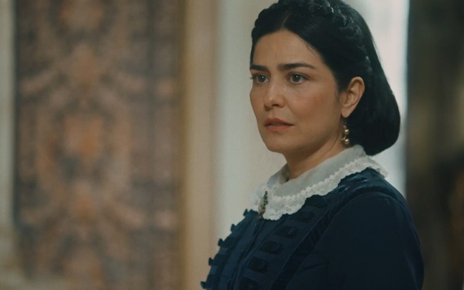 Leticia Sabatella grava com vestido azul escuro, cabelo preso e expressão de decepção e tristeza como Teresa de Nos Tempos do Imperador