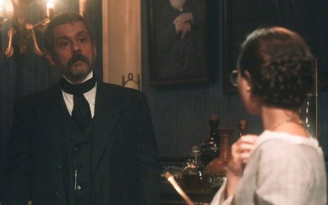 Tonico Rocha (Alexandre Nero) está em pé e observa joia no pescoço de Dolores (Daphne Bozaski) em cena de Nos Tempos do Imperador