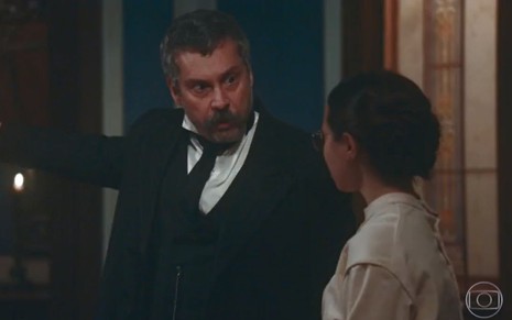 Tonico (Alexandre Nero) está em pé e gesticula com o braço para Dolores (Daphne Bozaski), ele tem expressão de raiva em cena de Nos Tempos do Imperador