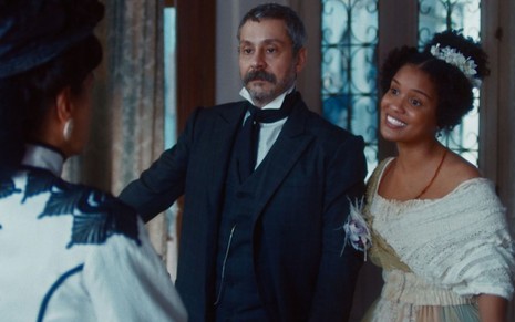Tonico (Alexandre Nero) e Zayla (Heslaine Vieira) estão de braços dados em cena de Nos Tempos do Imperador