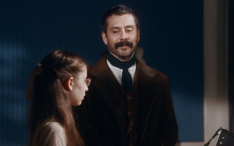 Tonico Rocha (Alexandre Nero) está em pé e conversa com Dolores (Júlia Freitas) em cena de Nos Tempos do Imperador