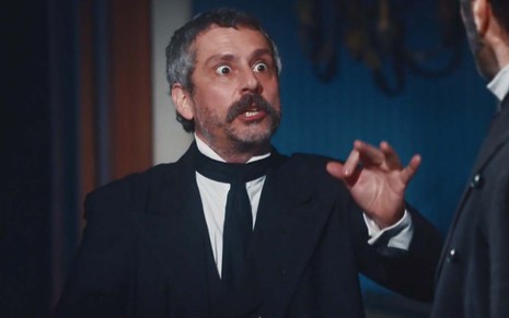 O ator Alexandre Nero como Tonico com expressão exaltada, como se brigasse com alguém, e mão direita em riste em cena de Nos Tempos do Imperador