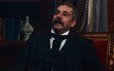 Tonico Rocha (Alexandre Nero) está sentado em mesa do seu gabinete em cena de Nos Tempos do Imperador
