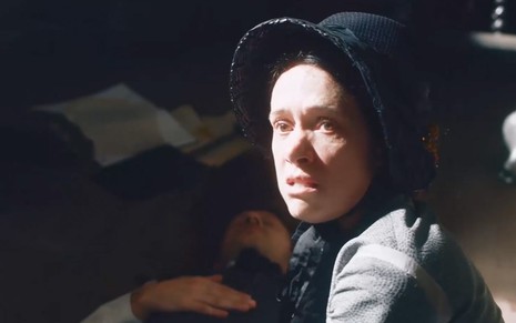 A atriz Bel Kutner caracterizada como Celestina com uma expressão furiosa em cena diurna de Nos Tempos do Imperador