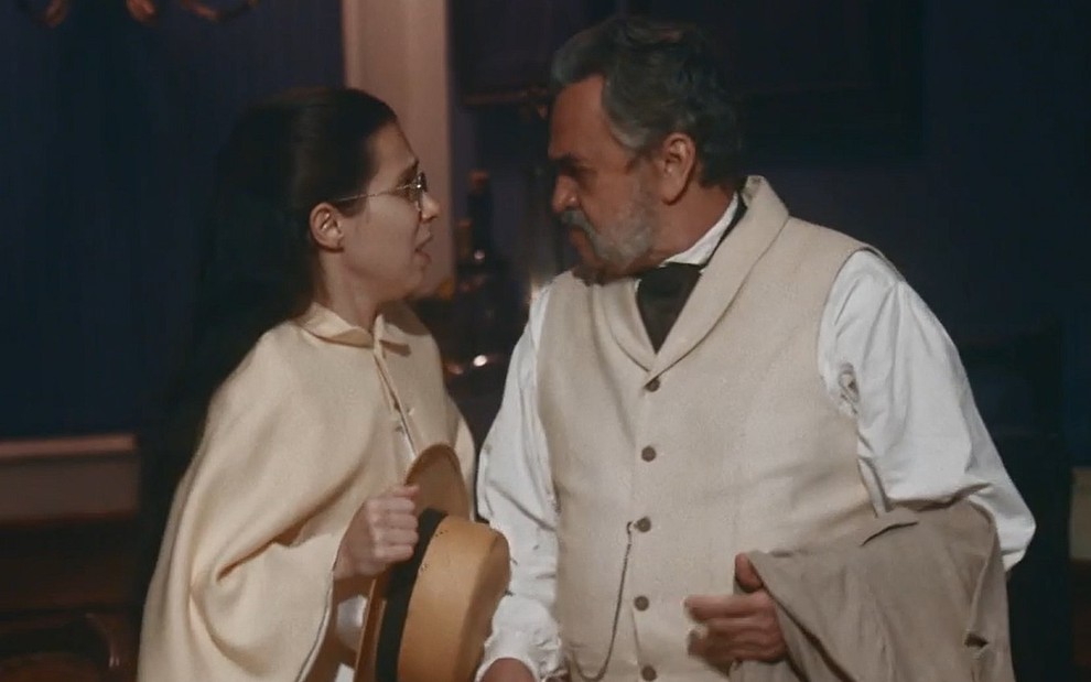 Dolores (Daphne Bozaski) e Eudoro (José Dumont) se encaram em Nos Tempos do Imperador, ambos estão com roupas de época brancas