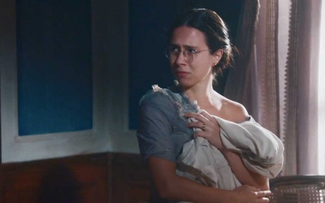 A atriz Daphne Bozaski como Dolores com expressão de choro segura um vestido branco aos trapos contra o corpo em cena de Nos Tempos do Imperador