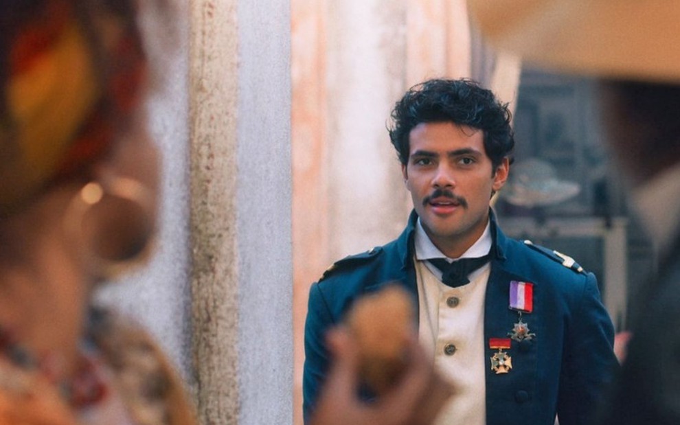Bernardinho (Gabriel Fuentes) está em pé em uma rua; ele usa o uniforme da Marinha em cena de Nos Tempos do Imperador