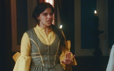 Pilar (Gabriela Medvedovski) está em pé e gesticula com a mão na sala de Dolores (Daphne Bozaski) em cena de Nos Tempos do Imperador