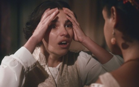Pilar (Gabriela Medvedovski) coloca as duas mãos na cabeça após e aparenta estar com raiva em cena de Nos Tempos do Imperador
