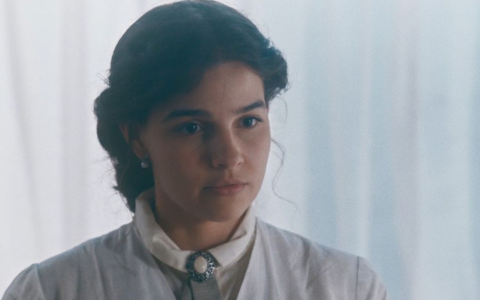 Pilar (Gabriela Medvedovski) está vestida com uniforme branco de médica em seu consultório na Ordem Terceira em cena de Nos Tempos do Imperador