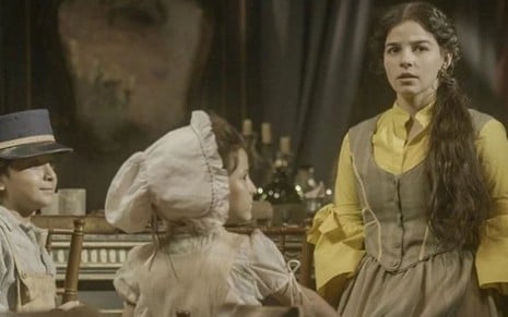 Pilar (Gabriela Medvedovski) está em pé ao lado de Prisca (Maria Carolina Basilio) e Hilário (Theo de Almeida) em cena no Hotel Cassino Perequetê, em Nos Tempos do Imperador