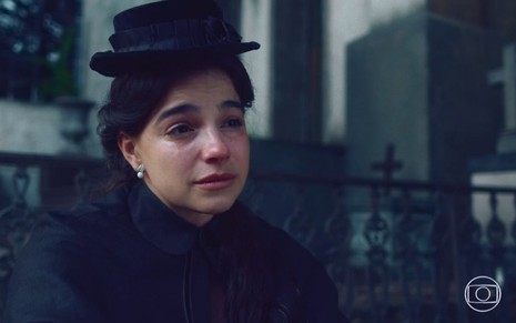 Pilar (Gabriela Medvedovski) chora; ela está vestida toda de preto e usa chapéu também preto em cena de Nos Tempos do Imperador