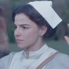 A atriz Gabriela Medvedovski com uniforme de enfermeira, na pele de Pilar, levanta as mãos para cima ao ser rendida em cena de Nos Tempos do Imperador