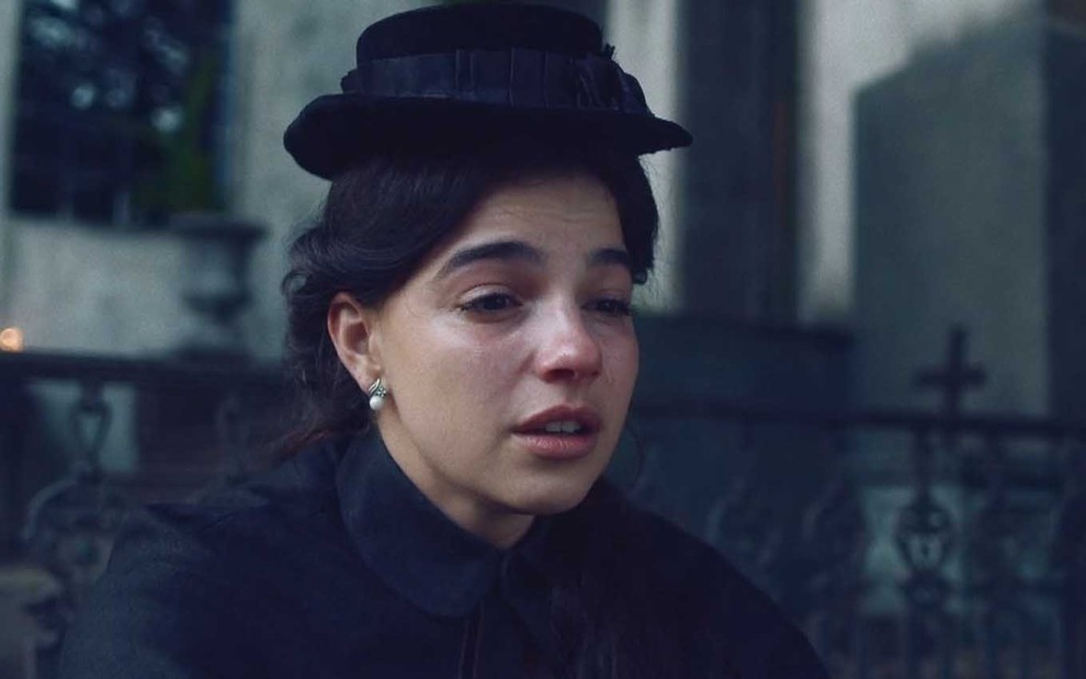 Pilar (Gabriela Medvedovski) chora; ela está vestida toda de preto e usa chapéu também preto em cena de Nos Tempos do Imperador
