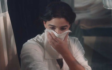 A atriz Gabriela Medevedovski leva um pano à boca diante de um leito hospitalar como a Pilar em cena de Nos Tempos do Imperador