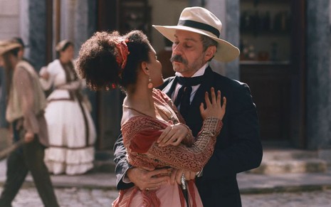 Heslaine Vieira e Alexandre Nero gravam cena abraçados, um olhando para o outro, como Zayla e Tonico